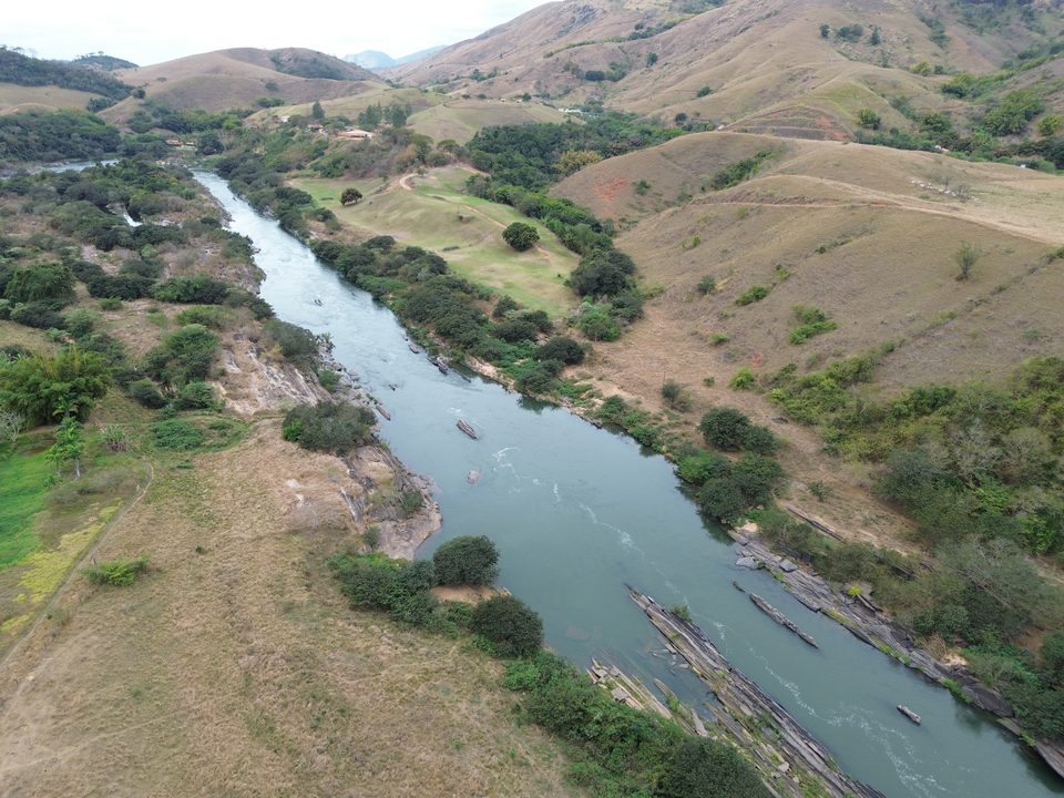 Leito rochoso do rio com vegetação nas margens e morros ao fundo