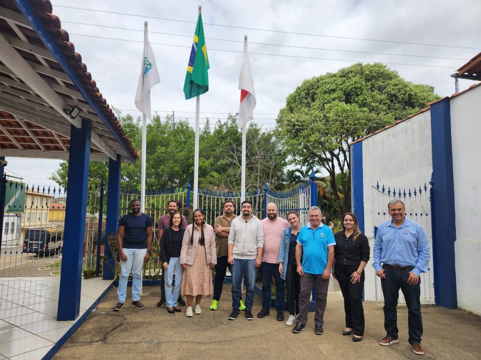 Equipe dos projetos e representantes da prefeitura reunidos em frente à sede municipal, sob as bandeiras do Brasil e de Minas Gerais