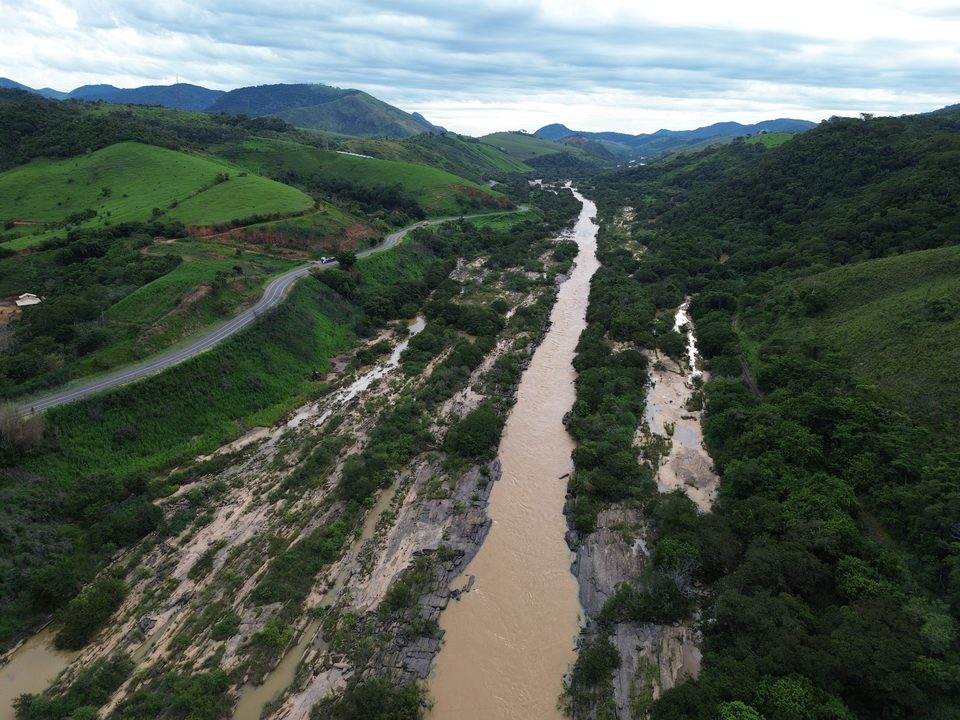 Rio com águas barrentas e volumosas entre encostas verdes sob céu nublado