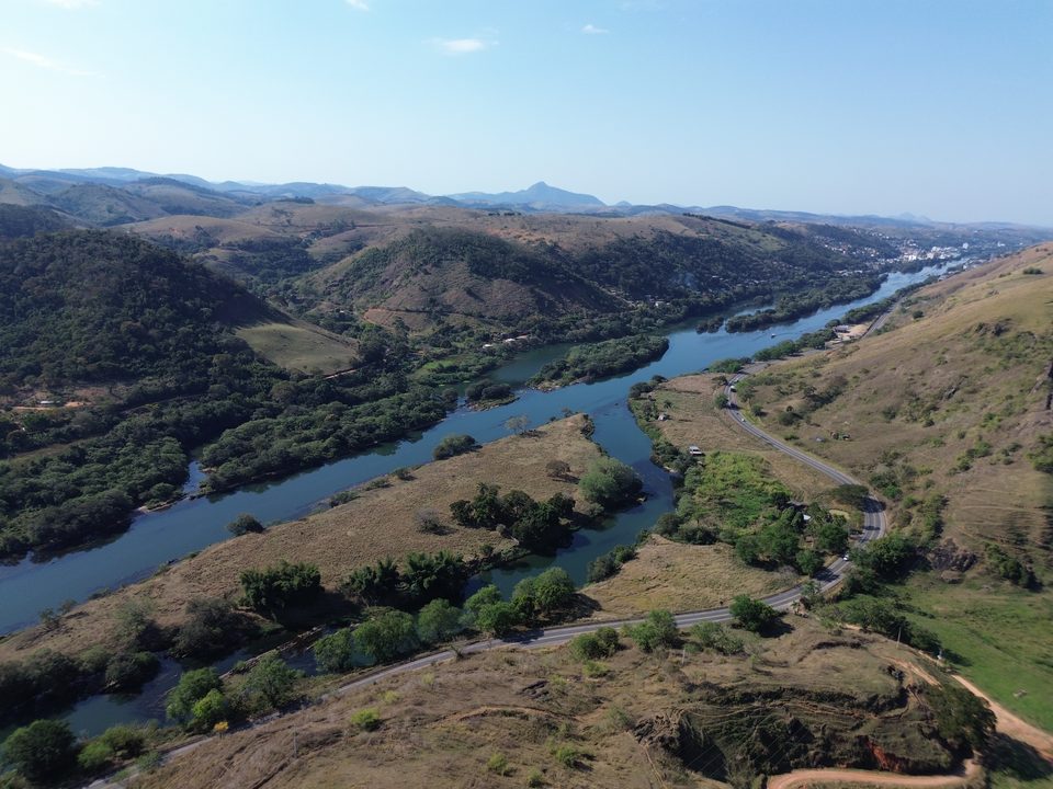 Vista aérea ampla do vale do Rio Paraíba do Sul, com a rodovia acompanhando a margem e morros ao fundo